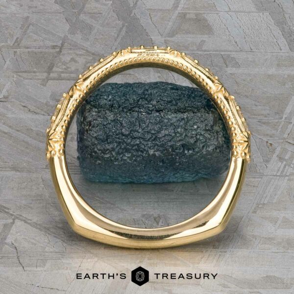 The "Marilyn" band in 18k yellow gold The "Marilyn" band in 18k yellow gold stands upright, encircling a rough blue stone on a textured grey background, with "Earth's Treasury" written below.