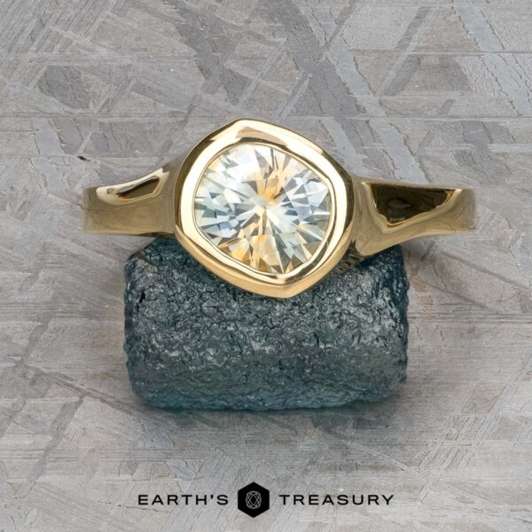 The "Winona" Ring in 18k yellow gold with 1.40-carat Montana sapphire The "Winona" Ring in 18k yellow gold with a 1.40-carat Montana sapphire is displayed on a rough blue stone, set against a textured gray background with "EARTH'S TREASURY" at the bottom—a treasure as captivating as its namesake.