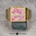 Introducing The Whitaker Ring in 18k yellow gold: a captivating piece with a square top adorned with unheated pink sapphires and clear gemstones on a textured background. This exquisite creation is a timeless blend of elegance and sophistication, perfect for any occasion.