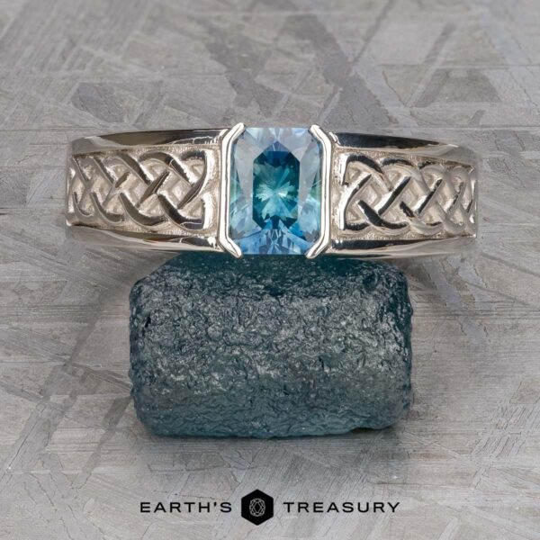 The "Shannon" ring in platinum with 1.06-Carat Montana Sapphire The "Shannon" ring in platinum, featuring a 1.06-carat Montana sapphire and Celtic knot designs, is shown on a rough blue-green stone with the EARTH'S TREASURY logo below.