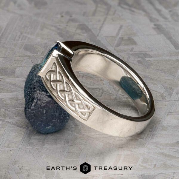 The "Shannon" ring in platinum with 1.06-Carat Montana Sapphire The "Shannon" ring in platinum with a 1.06-carat Montana Sapphire is shown leaning against a rough dark blue gemstone on a textured grey surface, with "EARTH'S TREASURY" displayed below.