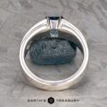 The "Shannon" ring in platinum with a 1.06-carat Montana Sapphire is displayed upright, highlighting the blue rectangular stone and band against a textured metallic background. The "Earth's Treasury" logo appears below.