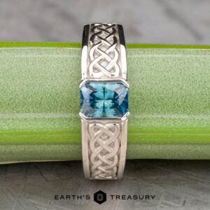 The "Shannon" ring in platinum, featuring a 1.06-carat Montana sapphire and detailed Celtic knotwork, is shown on a green stem with "Earth's Treasury" beneath.