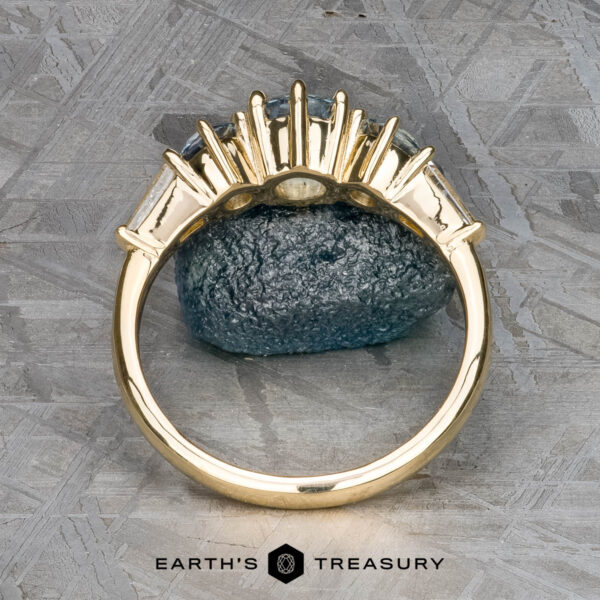 The "Concordia" ring in 14k yellow gold with 0.94-carat Montana sapphire The "Concordia" ring in 14k yellow gold, featuring a 0.94-carat Montana sapphire, is displayed upright against a rough bluish stone with a textured gray background.