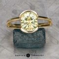 The "Madi" Ring in 14k yellow gold with a 2.56-carat Montana sapphire stands upright on a rough blue-green stone, set against a geometric background with "Earth's Treasury" written below.