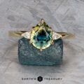 The "Sylph" ring in 14k yellow gold features a 1.62-carat pear-shaped Australian sapphire and two small diamonds, shown on a rough blue stone with the "Earth's Treasury" logo below.