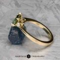 The "Sylph" ring in 14k yellow gold, featuring a 1.62-carat Australian sapphire, is shown leaning against a rough blue stone on a textured surface.