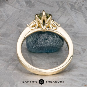 The "Sylph" ring in 14k yellow gold with a 1.62-carat Australian sapphire is shown upright in an ornate setting against a rough blue stone, with "Earth's Treasury" displayed below.
