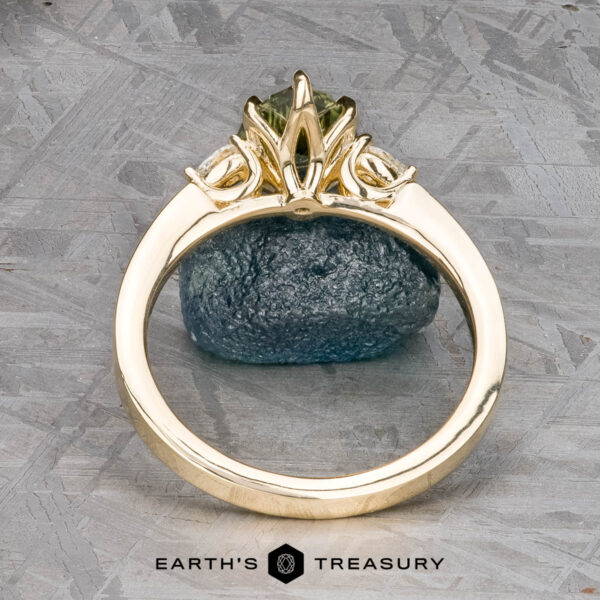 The "Sylph" ring in 14k yellow gold with 1.62-carat Australian sapphire The "Sylph" ring in 14k yellow gold with a 1.62-carat Australian sapphire is shown upright in an ornate setting against a rough blue stone, with "Earth's Treasury" displayed below.