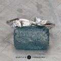 The "Lobelia" band in platinum, featuring five small white and light blue gemstones, is displayed on a rough blue stone with the "Earth's Treasury" logo below.