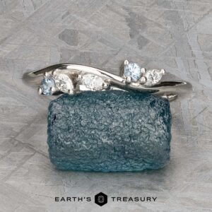 The "Lobelia" band in platinum, featuring five small white and light blue gemstones, is displayed on a rough blue stone with the "Earth's Treasury" logo below.