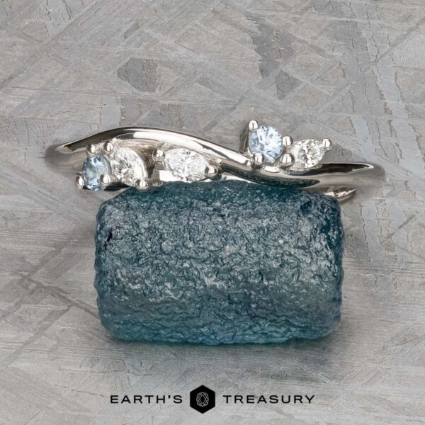 The "Lobelia" band in platinum The "Lobelia" band in platinum, featuring five small white and light blue gemstones, is displayed on a rough blue stone with the "Earth's Treasury" logo below.