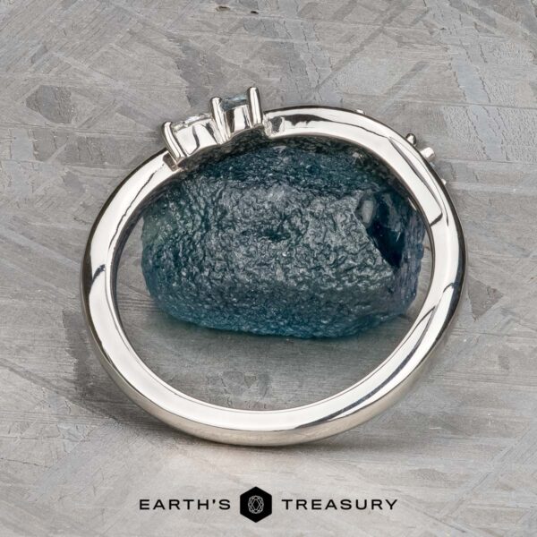 The "Lobelia" band in platinum The "Lobelia" band in platinum, featuring three rectangular gemstones, is displayed upright against a textured blue stone background with the Earth's Treasury logo at the bottom.