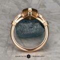 The "Myra" ring in 20k pink gold with a 0.81-carat Montana sapphire is displayed upright on a dark stone, set against a textured metallic background. The Earth's Treasury logo appears at the bottom.