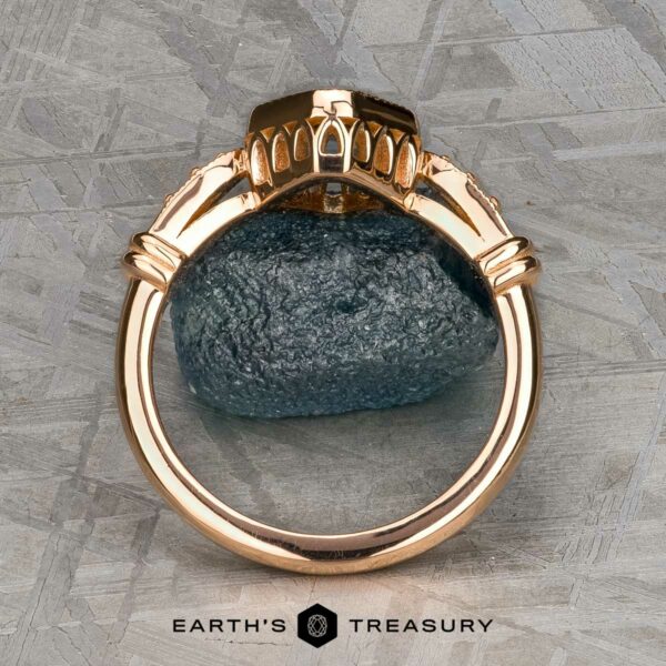 The "Myra" ring in 20k pink gold with 0.81-carat Montana sapphire The "Myra" ring in 20k pink gold with a 0.81-carat Montana sapphire is displayed upright on a dark stone, set against a textured metallic background. The Earth's Treasury logo appears at the bottom.