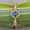 The "Myra" ring in 20k pink gold features a 0.81-carat square Montana sapphire and small round diamonds on the band, shown on a green leaf with the "Earth's Treasury" logo at the bottom.
