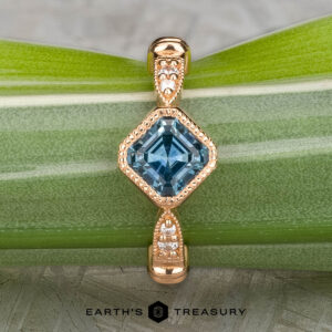 The "Myra" ring in 20k pink gold features a 0.81-carat square Montana sapphire and small round diamonds on the band, shown on a green leaf with the "Earth's Treasury" logo at the bottom.