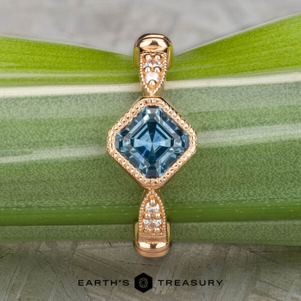 The "Myra" ring in 20k pink gold with 0.81-carat Montana sapphire The "Myra" ring in 20k pink gold features a 0.81-carat square Montana sapphire and small round diamonds on the band, shown on a green leaf with the "Earth's Treasury" logo at the bottom.