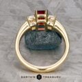 18k yellow gold "Olympia" ring featuring a 1.18-carat ruby and clear stones on a textured surface, labeled "Earth's Treasury.