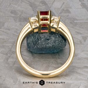 18k yellow gold "Olympia" ring featuring a 1.18-carat ruby and clear stones on a textured surface, labeled "Earth's Treasury.