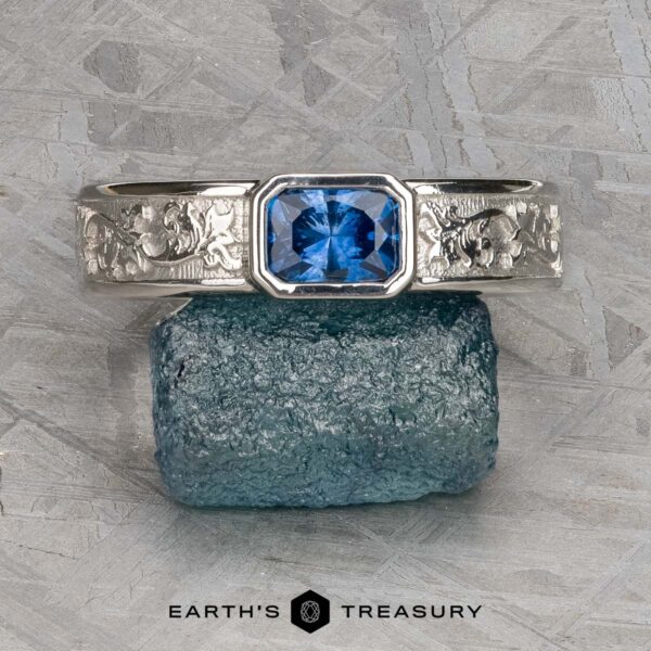 The "Kittley" ring in platinum with 0.80-carat Montana Sapphire The "Kittley" ring in platinum features a 0.80-carat Montana Sapphire and an engraved band, shown on a rough blue stone with the Earth's Treasury logo beneath.