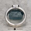 The "Kittley" ring in platinum with a 0.80-carat Montana Sapphire rests on a textured gray surface over a rough blue gemstone. "EARTH'S TREASURY" below underscores the unique jewelry and fashion elegance of this piece.