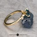 The "Poppy" ring in 18k yellow gold, featuring a 0.98-carat Montana sapphire and small diamonds, is displayed on a rough, dark stone surface. The logo "EARTH'S TREASURY" appears at the bottom of the image.