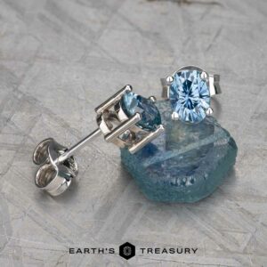 The EA-MS-438 stud earring, featuring a blue gemstone, is displayed on a matching raw crystal with the "Earth's Treasury" logo at the bottom.