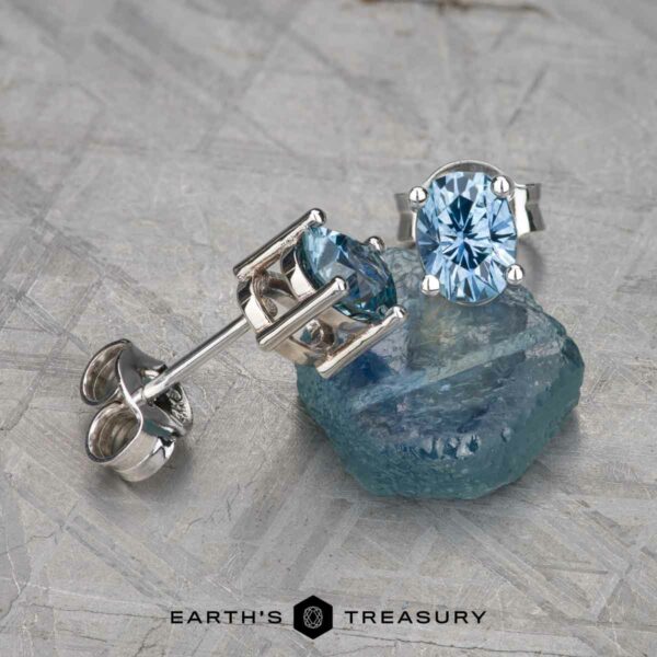 EA-MS-438 The EA-MS-438 stud earring, featuring a blue gemstone, is displayed on a matching raw crystal with the "Earth's Treasury" logo at the bottom.
