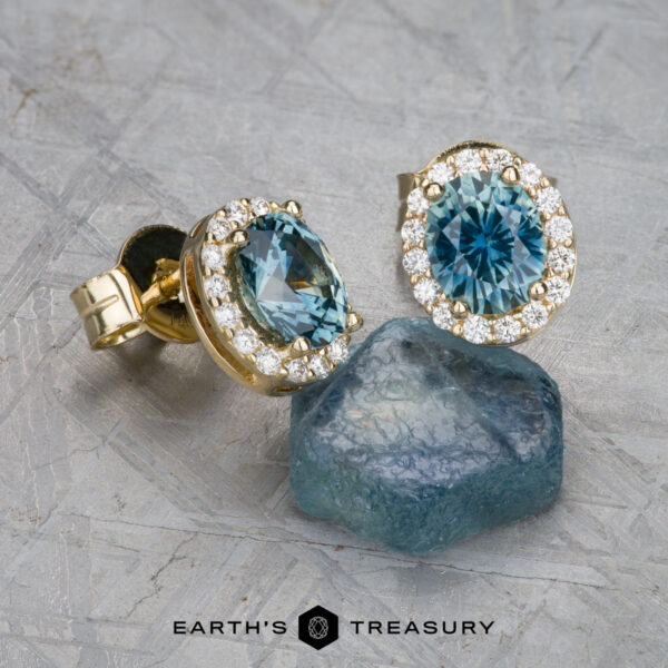 EA-MS-523 The EA-MS-523 earrings, featuring blue gemstones and diamond accents, are showcased alongside a rough blue stone on a textured surface. Text at the bottom reads "Earth's Treasury.