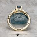 The "Viney" ring in 14k yellow gold with a 0.76-carat Montana sapphire is displayed upright on a textured gray surface, with "EARTH'S TREASURY" written below.