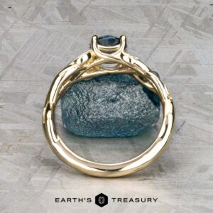The "Viney" ring in 14k yellow gold with a 0.76-carat Montana sapphire is displayed upright on a textured gray surface, with "EARTH'S TREASURY" written below.