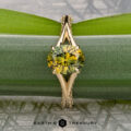 The "Antoinette" ring features a 1.69-carat Australian yellow-green sapphire in 14k yellow gold with a split-shank setting, shown on a green leaf with "Earth's Treasury" branding below.