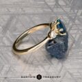 The "Nymph" ring in 14K yellow gold features a 1.27-carat Montana sapphire accented by two pear-shaped clear stones, displayed on a rough blue crystal with the "Earth’s Treasury" logo—a striking three-stone ring for any occasion.