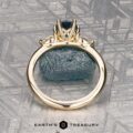 The "Nymph" ring in 14K yellow gold features a 1.27-carat Montana sapphire accented by two pear-shaped clear stones, displayed on a rough blue crystal with the "Earth’s Treasury" logo—a striking three-stone ring for any occasion.