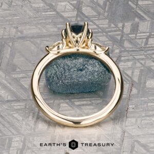 The "Nymph" ring in 14K yellow gold features a 1.27-carat Montana sapphire accented by two pear-shaped clear stones, displayed on a rough blue crystal with the "Earth’s Treasury" logo—a striking three-stone ring for any occasion.