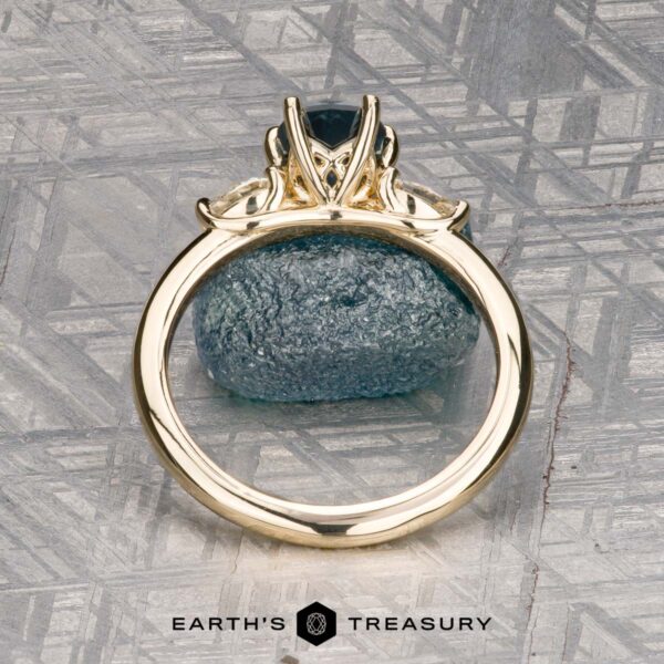 The "Nymph" ring in 14K yellow gold with 1.27-carat Montana sapphire The "Nymph" ring in 14K yellow gold features a 1.27-carat Montana sapphire accented by two pear-shaped clear stones, displayed on a rough blue crystal with the "Earth’s Treasury" logo—a striking three-stone ring for any occasion.
