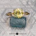 The "Anise" ring in 14K yellow gold with a 2.43-carat Australian sapphire features leaf-shaped side accents and is shown on a rough blue-green stone with a patterned gray background. The "Earth's Treasury" logo appears at the bottom.