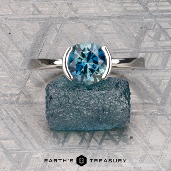 The "Lina" ring in platinum with 1.83-carat Montana sapphire The "Lina" ring in platinum with a 1.83-carat Montana sapphire is displayed on textured blue stone, with the "EARTH'S TREASURY" logo beneath.