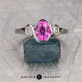 The "Kaelin" ring in 14K white gold features a 1.53-carat oval Ceylon sapphire flanked by two clear stones, displayed on a rough blue-green crystal with the "Earth's Treasury" logo below.