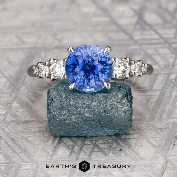 The "Celosia" ring in 18K white gold with 3.06-carat Ceylon sapphire The "Celosia" ring in 18K white gold features a 3.06-carat Ceylon sapphire and diamond accents, shown on a rough gemstone with "Earth's Treasury" branding—a refined, elegant design.