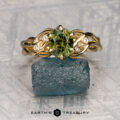 The "Viney" ring in 18k yellow gold features a 1.55-carat Australian sapphire, four small diamonds, and leaf motifs on the band; it rests on a rough blue stone with the "Earth's Treasury" logo below.
