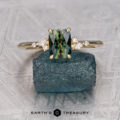The "Iris" ring in 18K yellow gold with a 1.23-carat Australian sapphire is shown on a rough blue crystal, flanked by two clear stones, with the "Earth's Treasury" logo below.