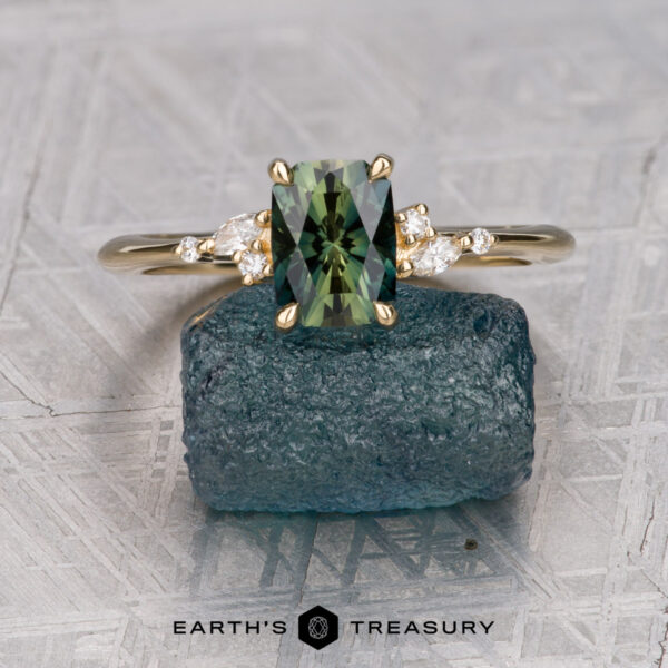 The "Iris" ring in 18K yellow gold with 1.23-carat Australian sapphire The "Iris" ring in 18K yellow gold with a 1.23-carat Australian sapphire is shown on a rough blue crystal, flanked by two clear stones, with the "Earth's Treasury" logo below.