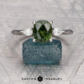 The "Dryad" ring in 18K white gold, featuring a 2.21-carat Australian sapphire and two clear side stones, is displayed on a rough blue crystal with the "Earth's Treasury" logo at the bottom.