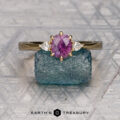 The "Sylph" ring in 18K yellow gold, set with a 0.94-carat Montana sapphire and two white stones, is showcased on a rough blue crystal against a geometric patterned background.