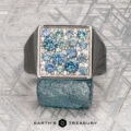 The "Whitaker" ring in platinum features a square face set with blue gemstones, shown on a rough blue mineral with "Earth's Treasury" below.