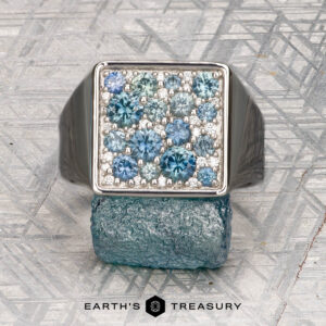 The "Whitaker" ring in platinum features a square face set with blue gemstones, shown on a rough blue mineral with "Earth's Treasury" below.