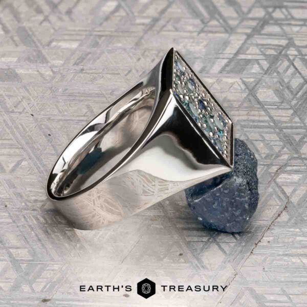 The "Whitaker" ring in platinum The "Whitaker" ring in platinum features a square face set with blue gemstones, shown on a rough blue mineral with "Earth's Treasury" below.