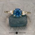 The "Iris" ring in 14K yellow gold with a 1.60-carat Montana sapphire stands upright against a rough blue stone, with the "Earth's Treasury" logo below on a textured background.